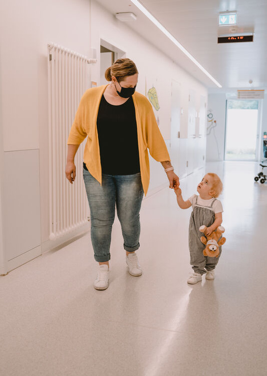 Herzkind Emilia au dem Flur in der Klinik an der Hand ihrer Mutter