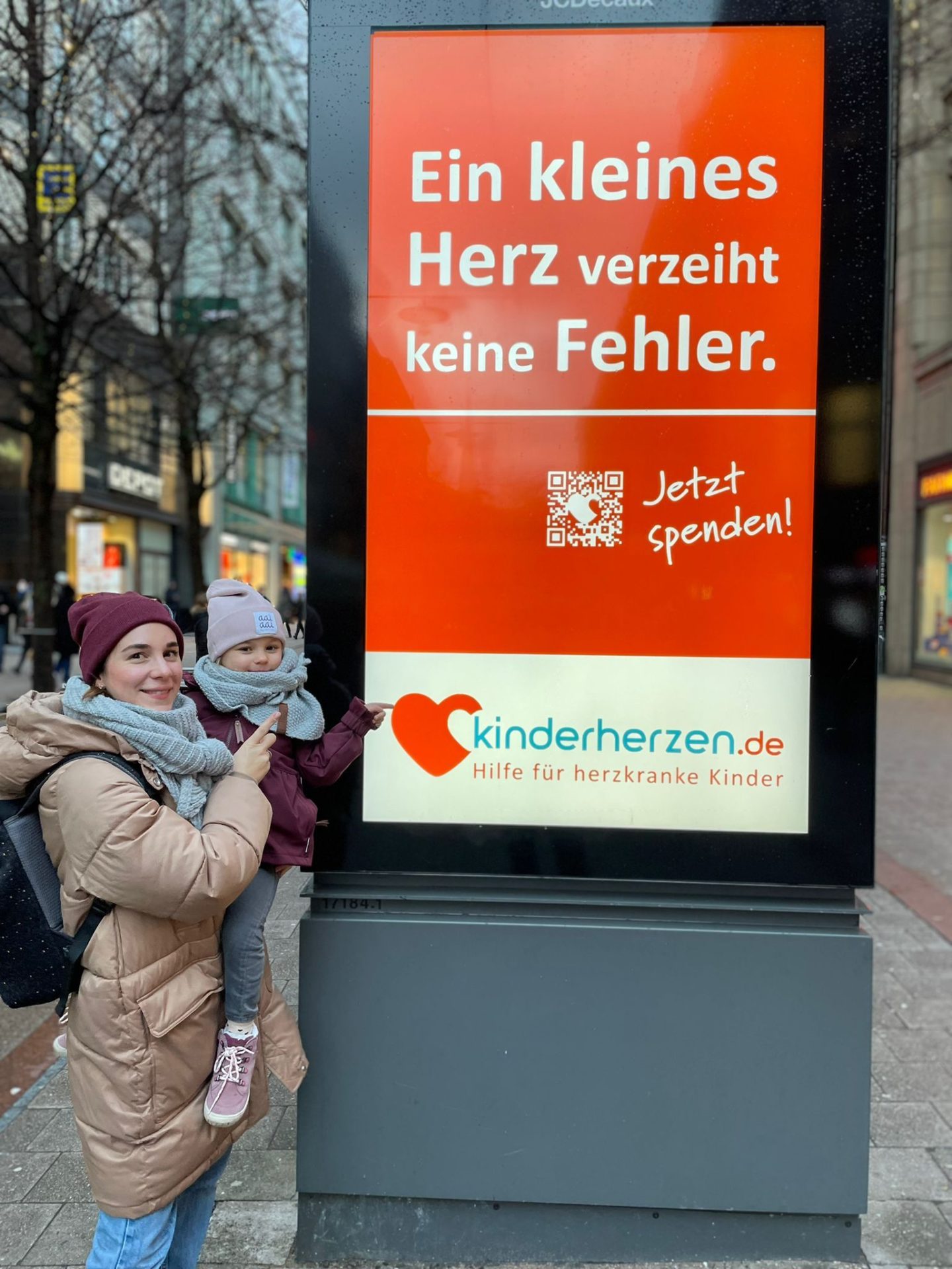 Herzkind Firda mit Mutter vor einem Plakat von kinderherzen 